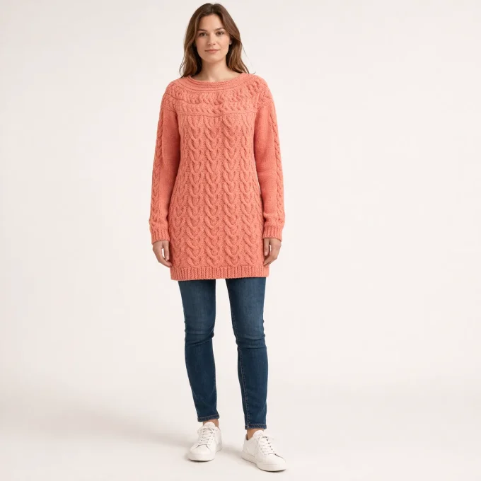 Pull long corail pour femme en tricot a torsades avec col rond porte de face avec un jean bleu et de